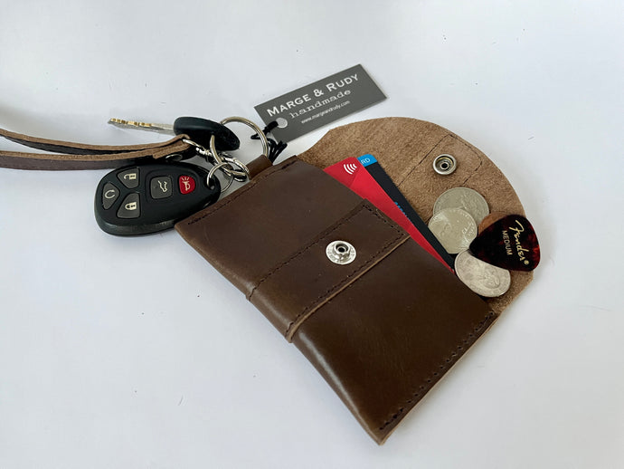 Handcrafted genuine leather keychain wallet with wristlet strap in brown shown open with keys attached and cards, coins and guitar pick inside.
